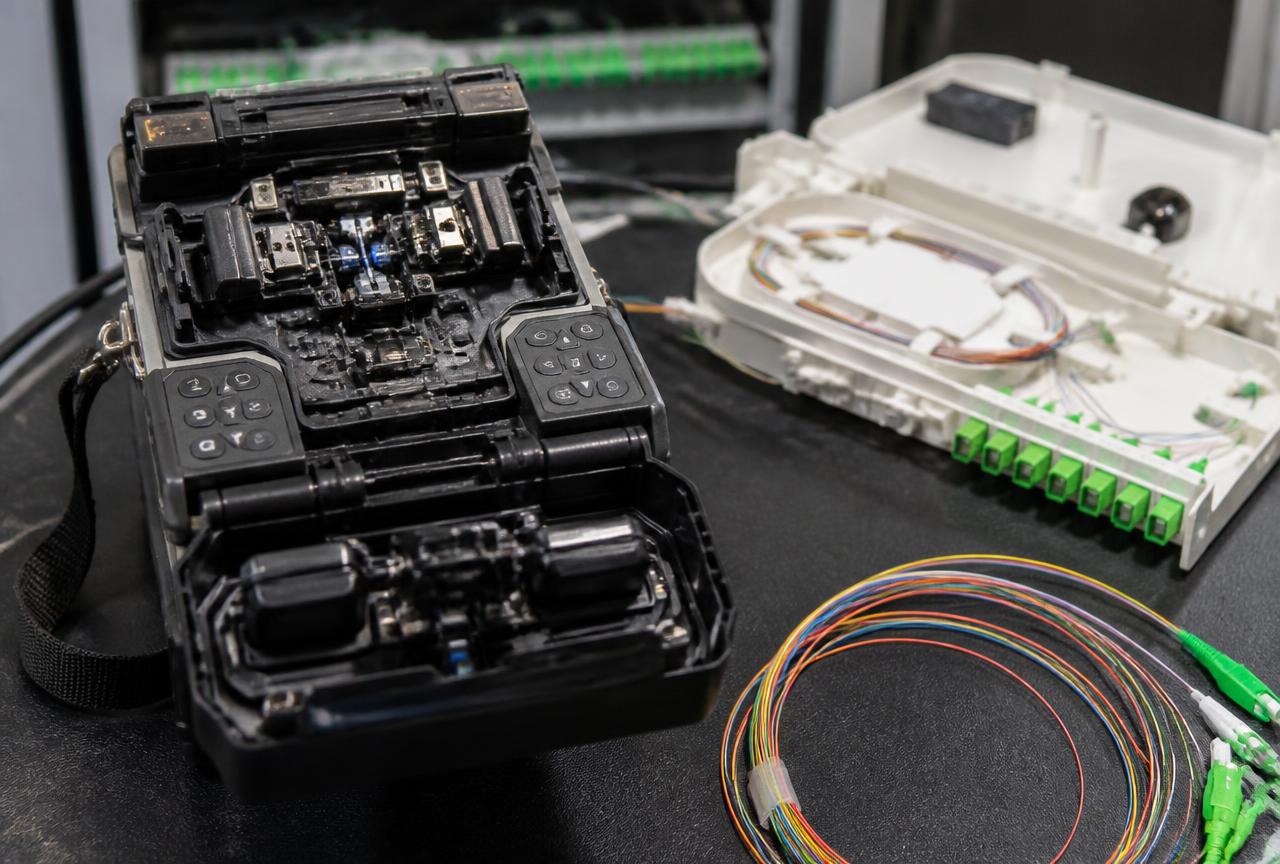 Fibre optic fusion splicing machine beside a splice tray, coloured pigtails and an optical fibre distribution panel