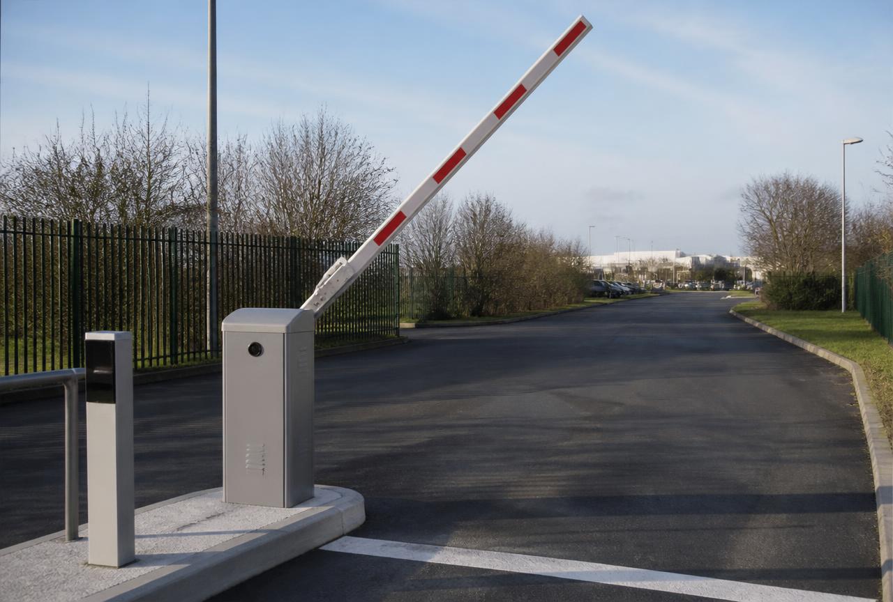 Boom barrier gate raised at an industrial site vehicle entrance with a reader pedestal beside the lane